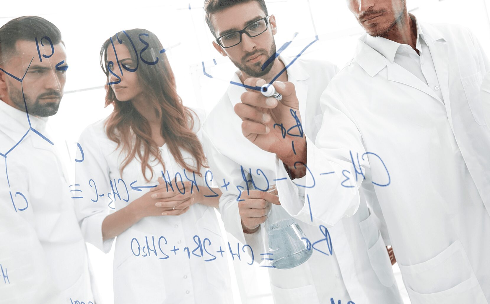 A group of people in lab coats engaged in Special IBE Membership research while writing on a white board.