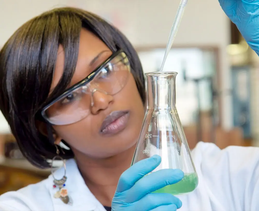 A female scientist from the Institute of Biological Engineering holds a beaker of green liquid.